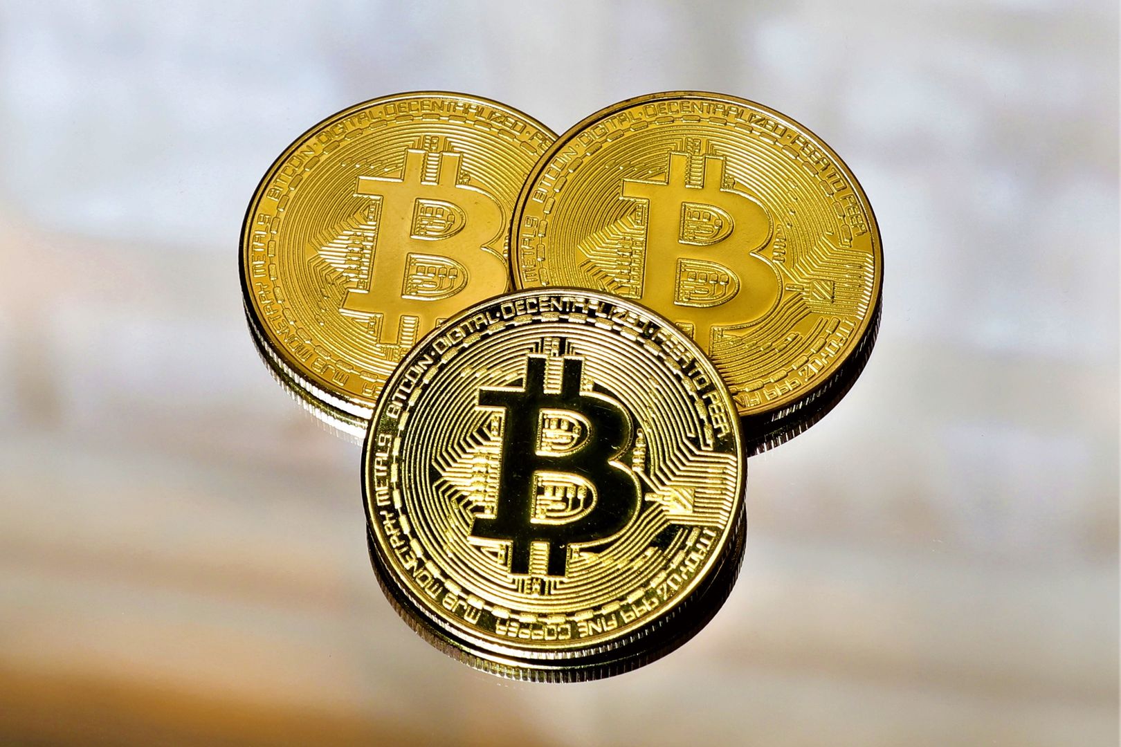 Close-up of three gold Bitcoin coins on a reflective surface highlighting cryptocurrency and finance.