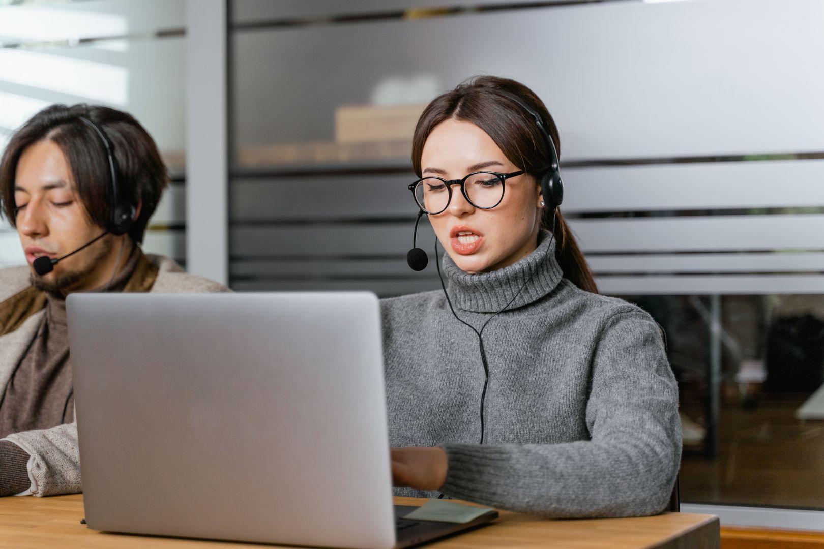 Customer support agents wearing headsets working on laptops in a modern office setting.